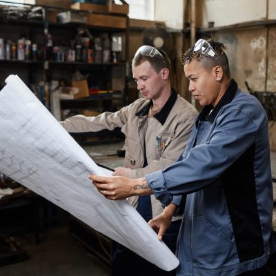 Two People Looking At Plans In Factory Workshop